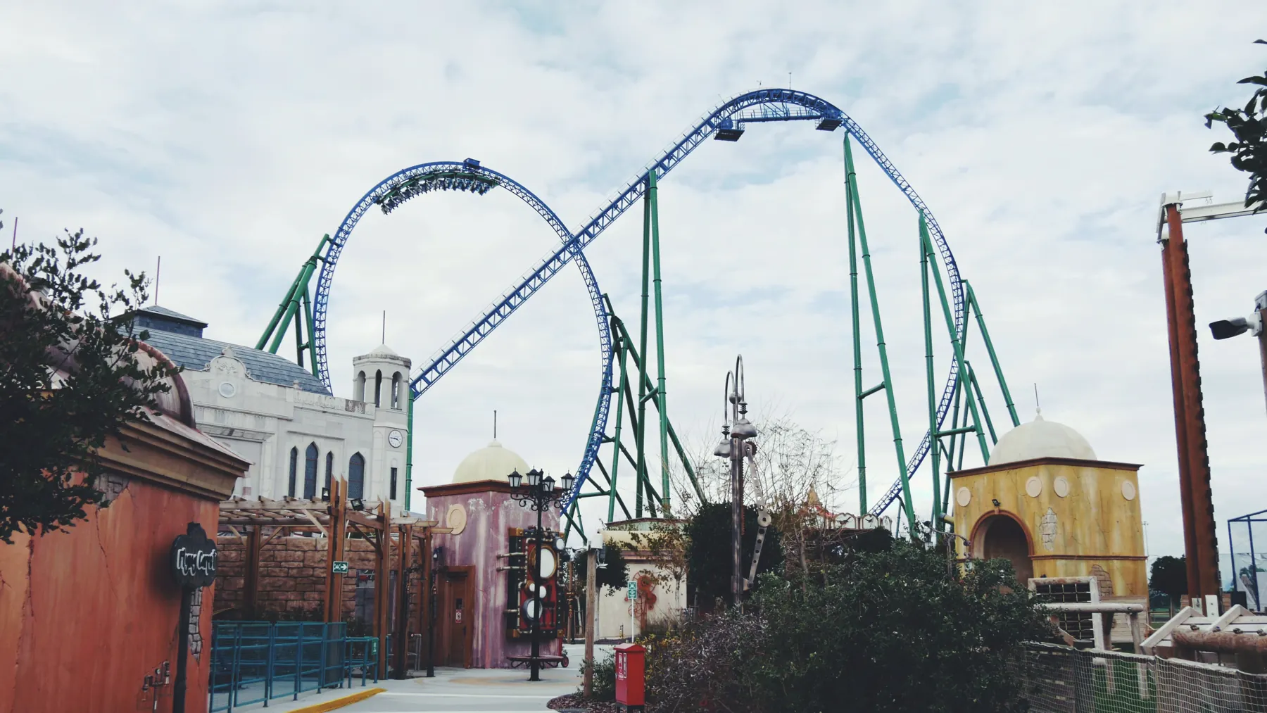 The blue and green track of the Hyper Coaster looping above pastel buildings under a cloudy sky