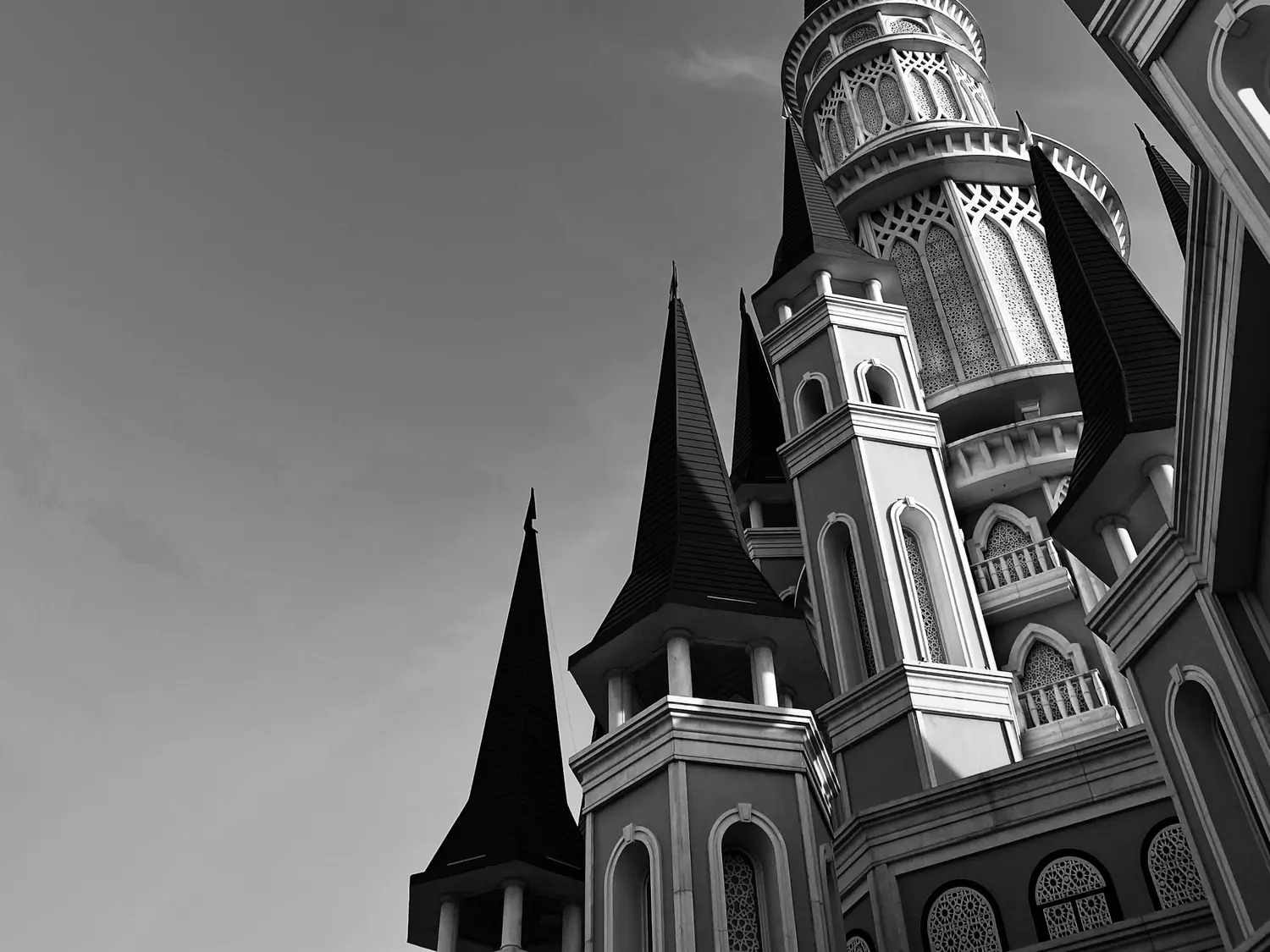 Black-and-white view up at the spired towers of the castle, with a round tower of carved arches against a cloudy sky